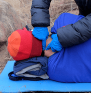 Student wearing gloves practices taking the pulse of another student during a simulation.